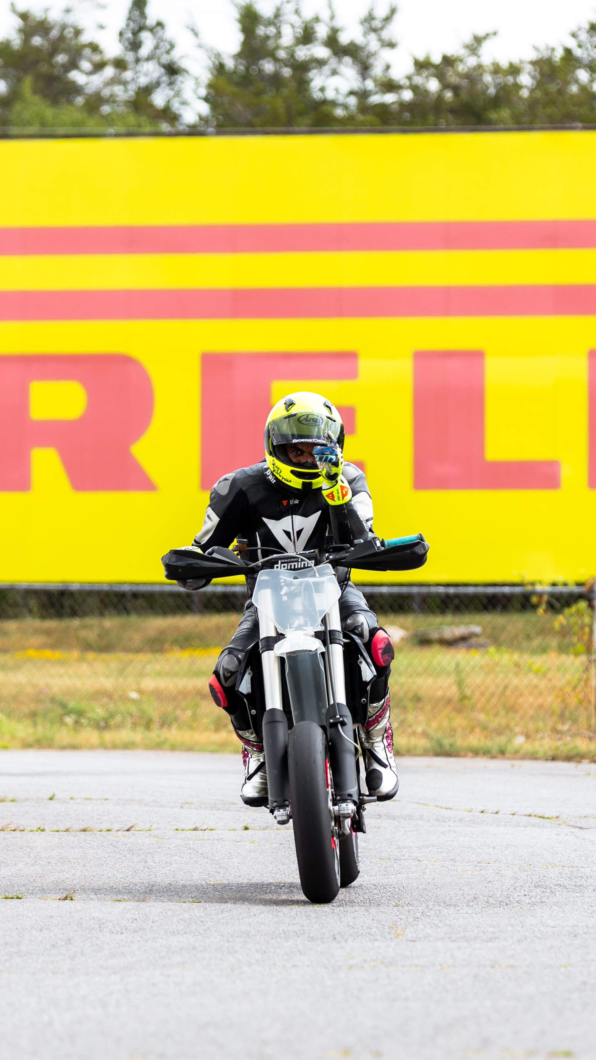 A yellow-helmeted supermoto rider approaching beneath a Pirelli sign.