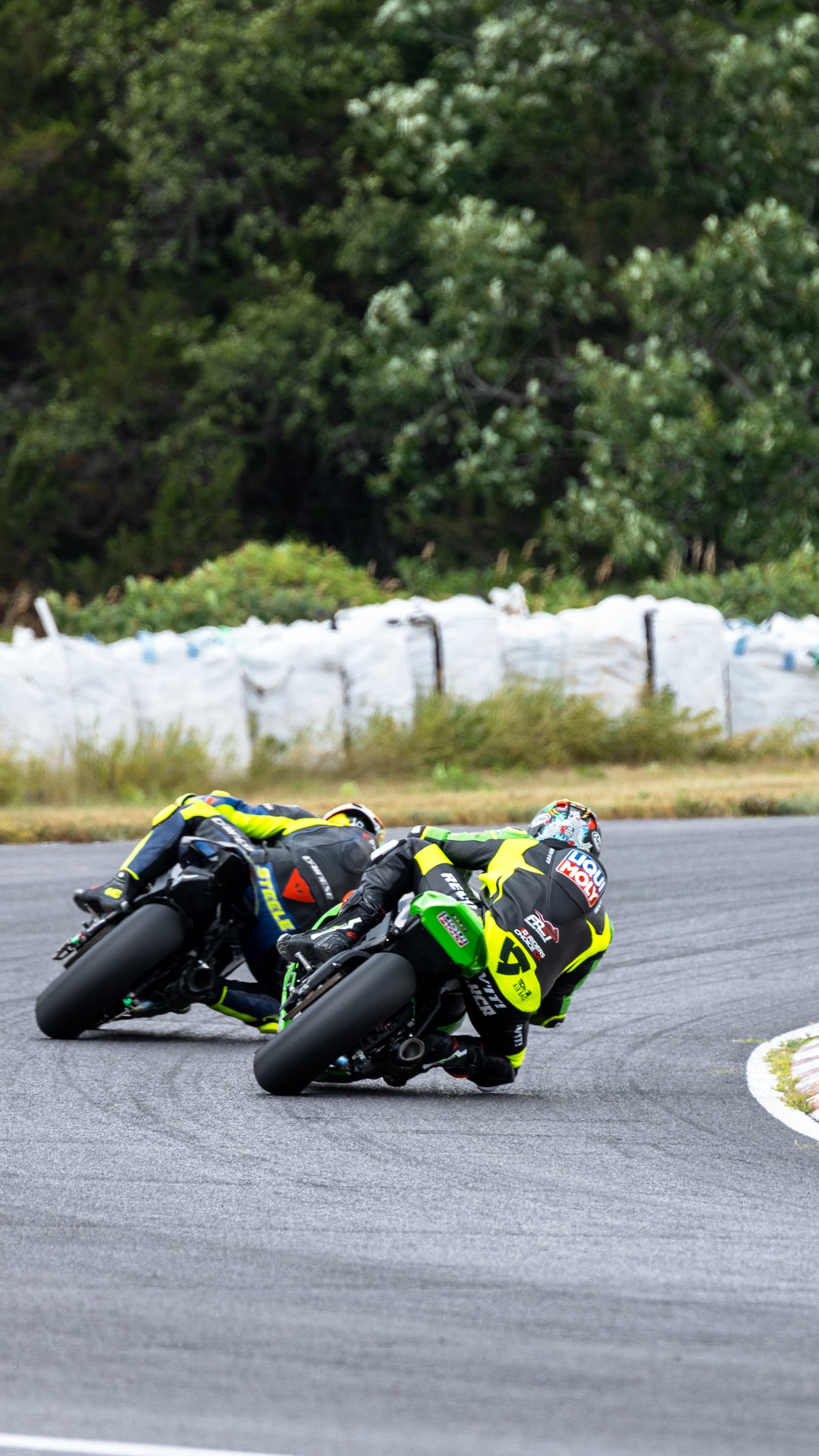 Two motorcycle riders leaning through a corner, seen from behind.
