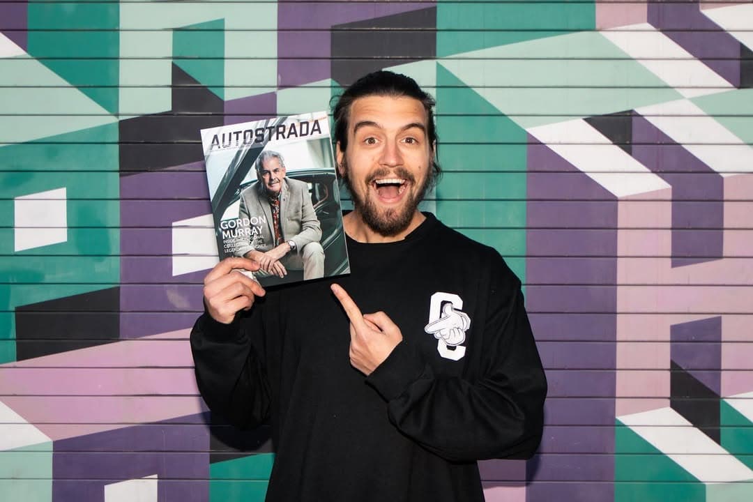 Holding an Autostrada Magazine issue featuring Gordon Murray, in front of a colourful mural.