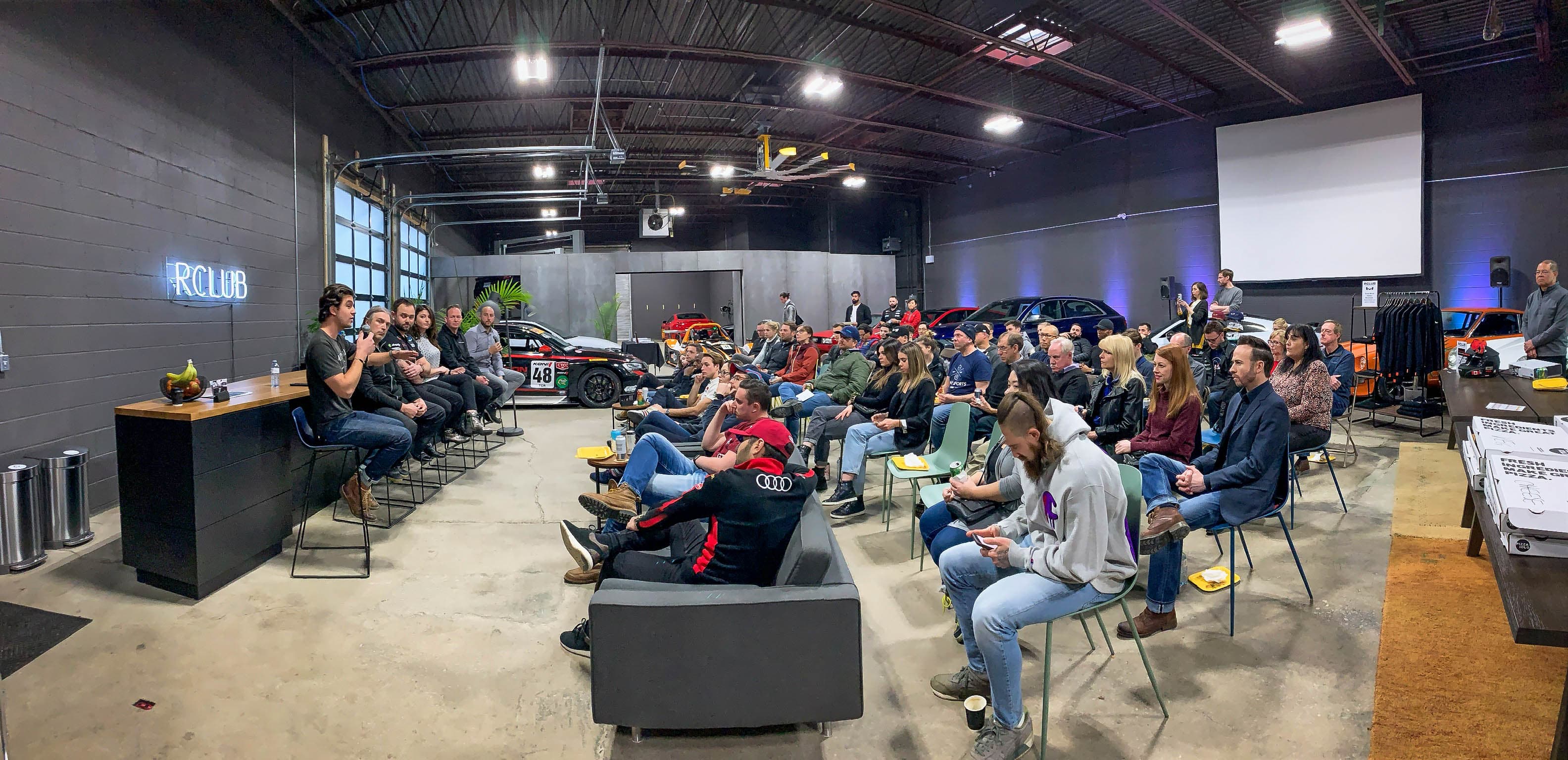 A live panel conversation surrounded by cars and an audience at RCLUB.