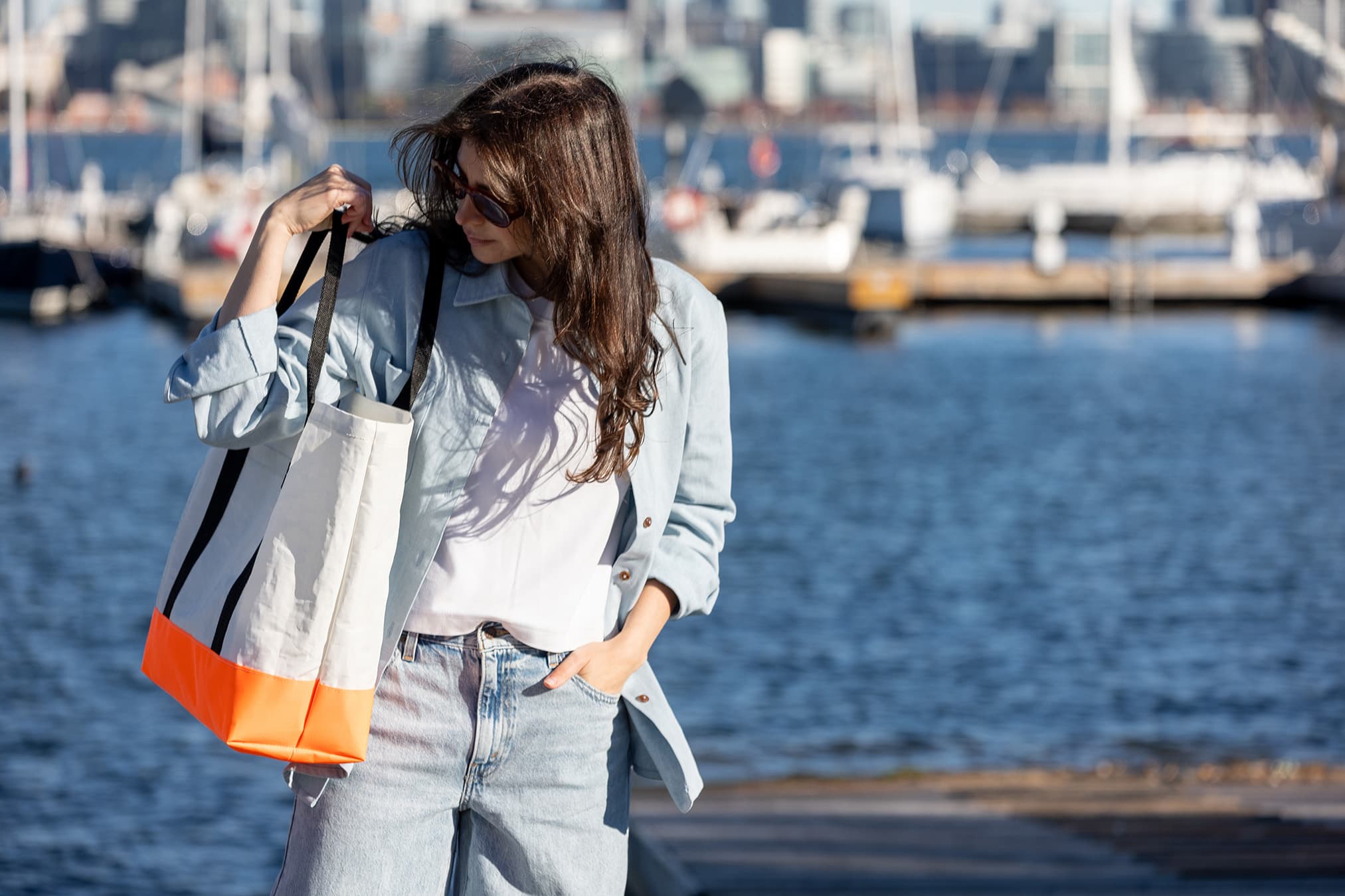 A model holding a Dayshaped tote beside the water and sailboats.