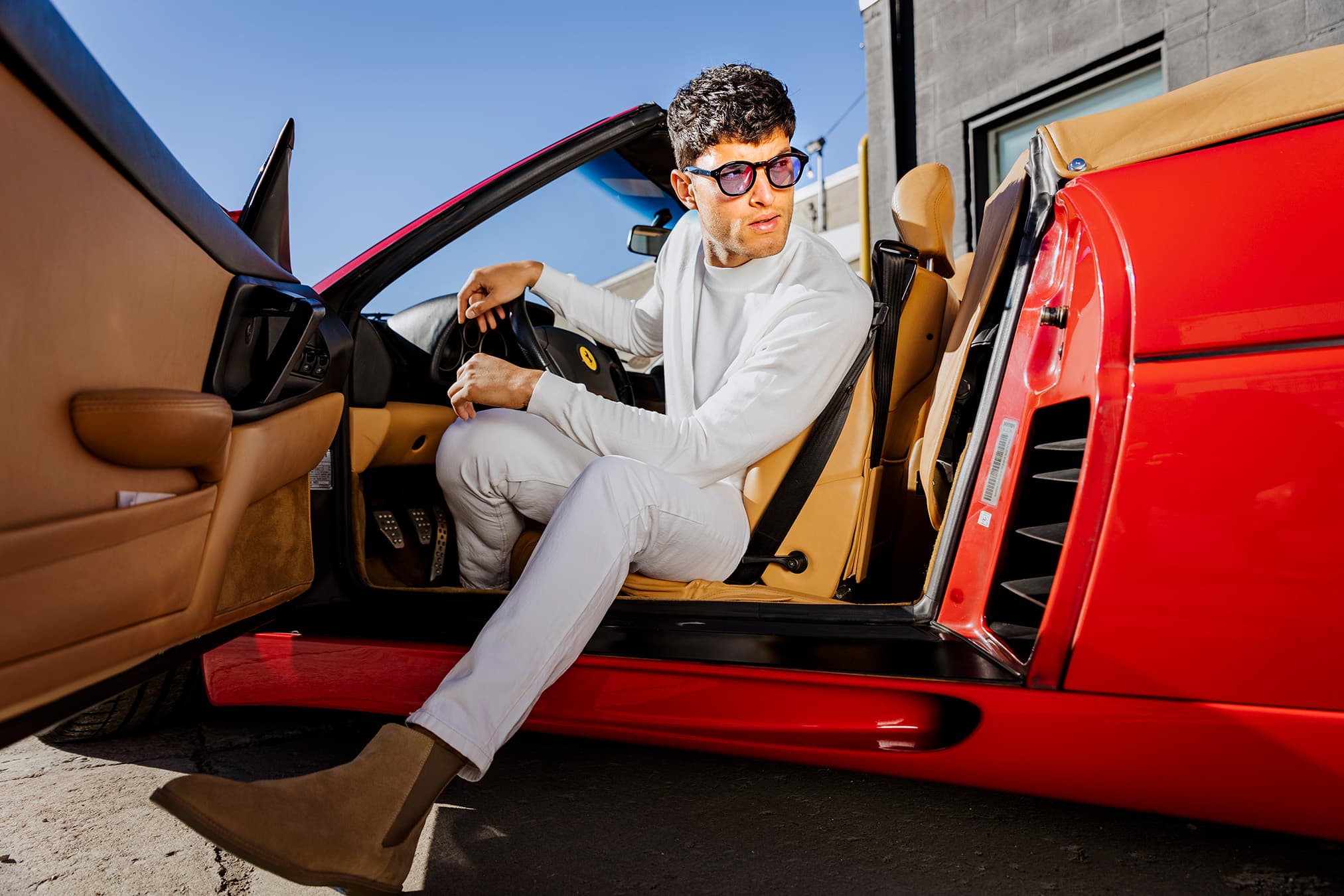 A model wearing Waid sunglasses seated in a red Ferrari convertible.