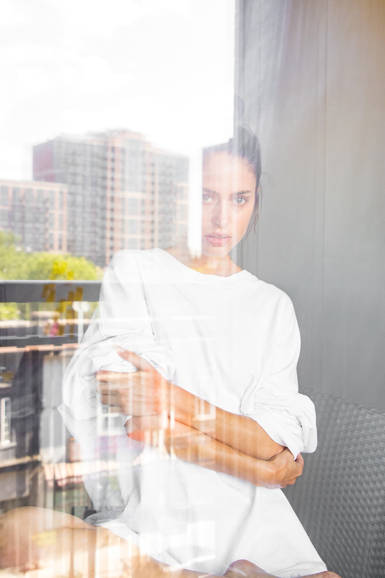 Chloe seated behind reflective window glass with buildings reflected across her portrait.