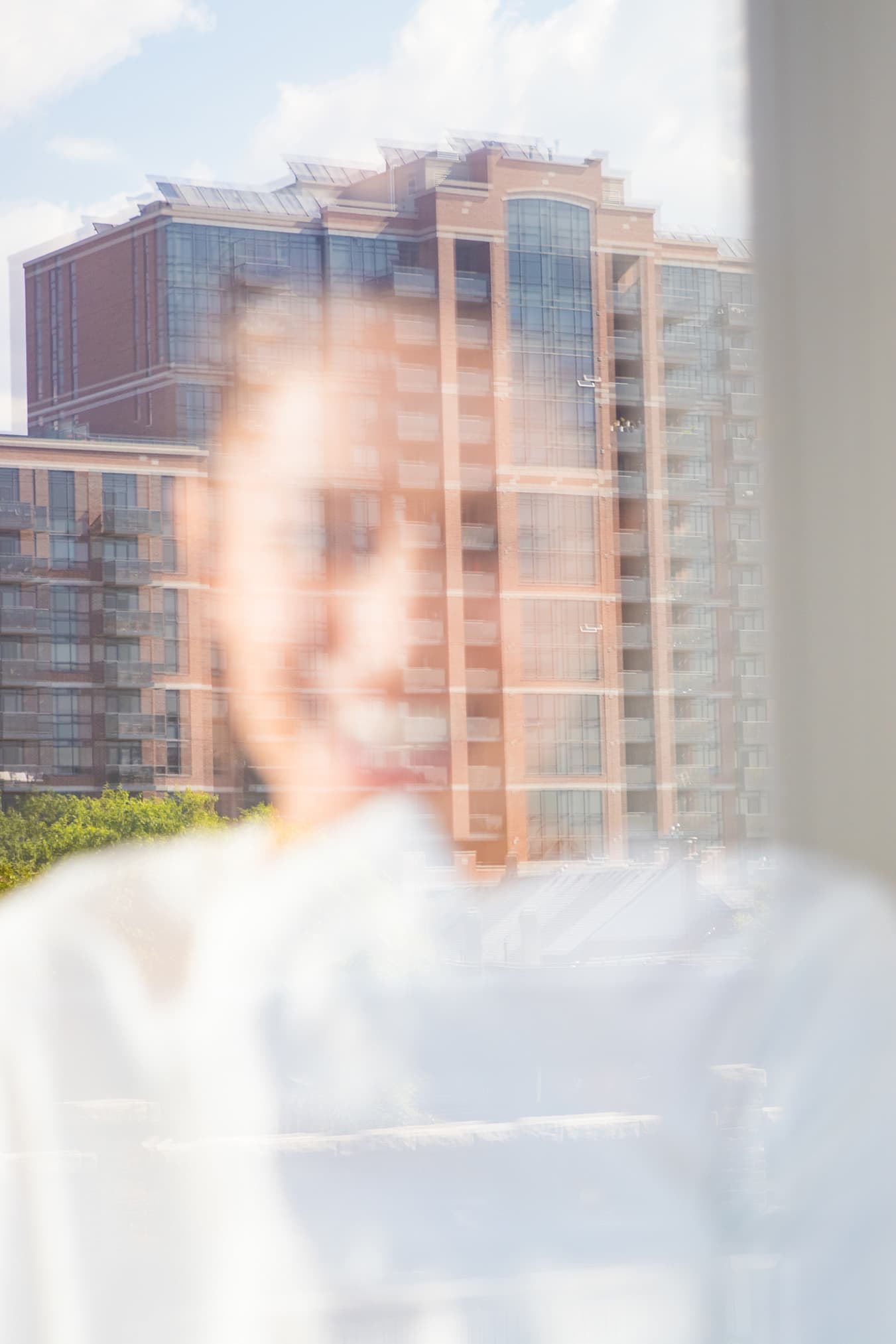 Chloe softly out of focus behind glass reflecting a brick building and sky.