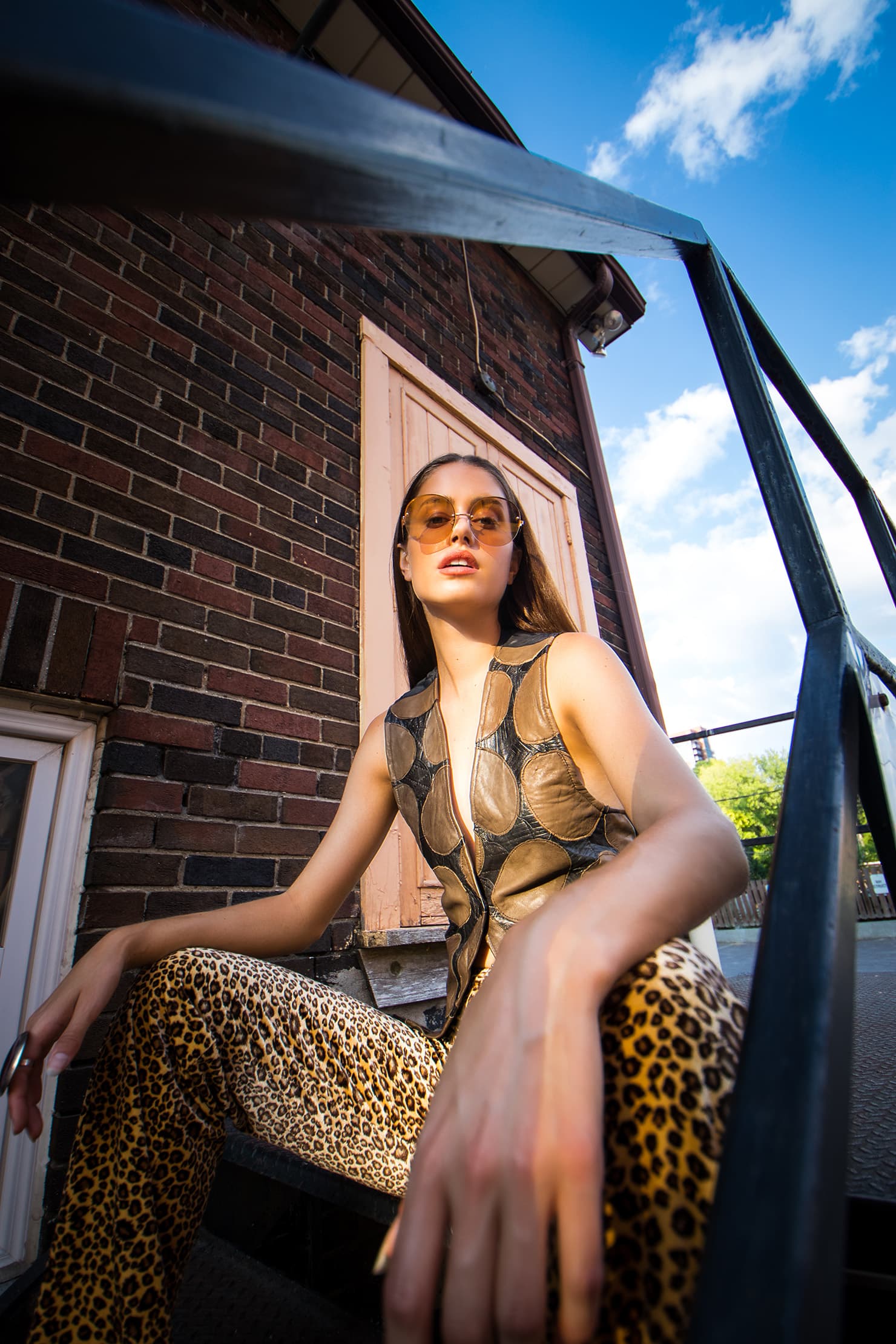 Chloe wearing amber sunglasses and leopard-print trousers on outdoor steps.