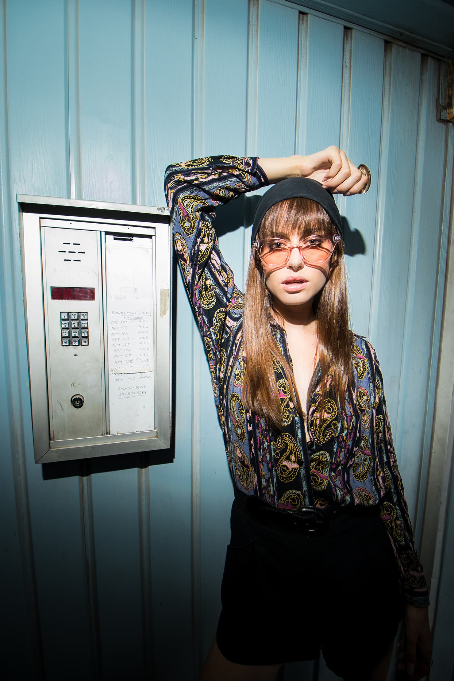 Chloe in a patterned blouse and tinted glasses beside a blue doorway.