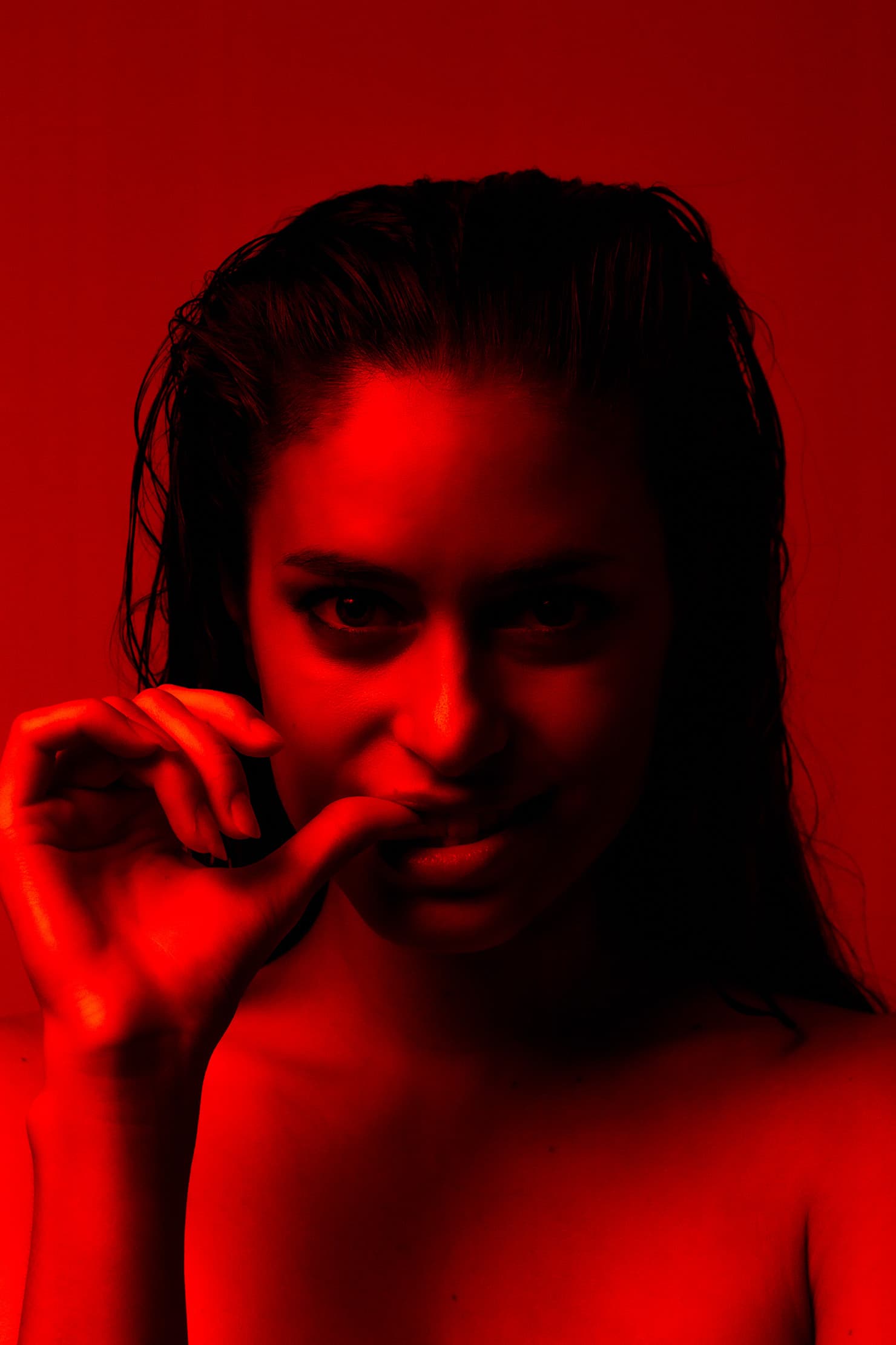 Red-lit portrait of Chloe looking at the camera with her hand near her lips.