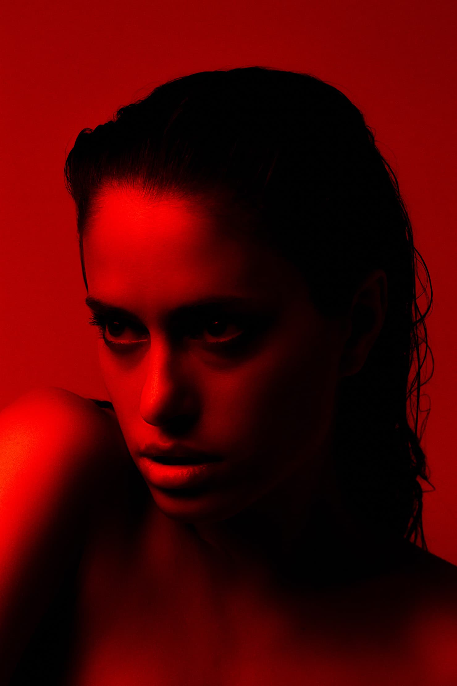 Red-lit close portrait of Chloe looking past her raised shoulder.