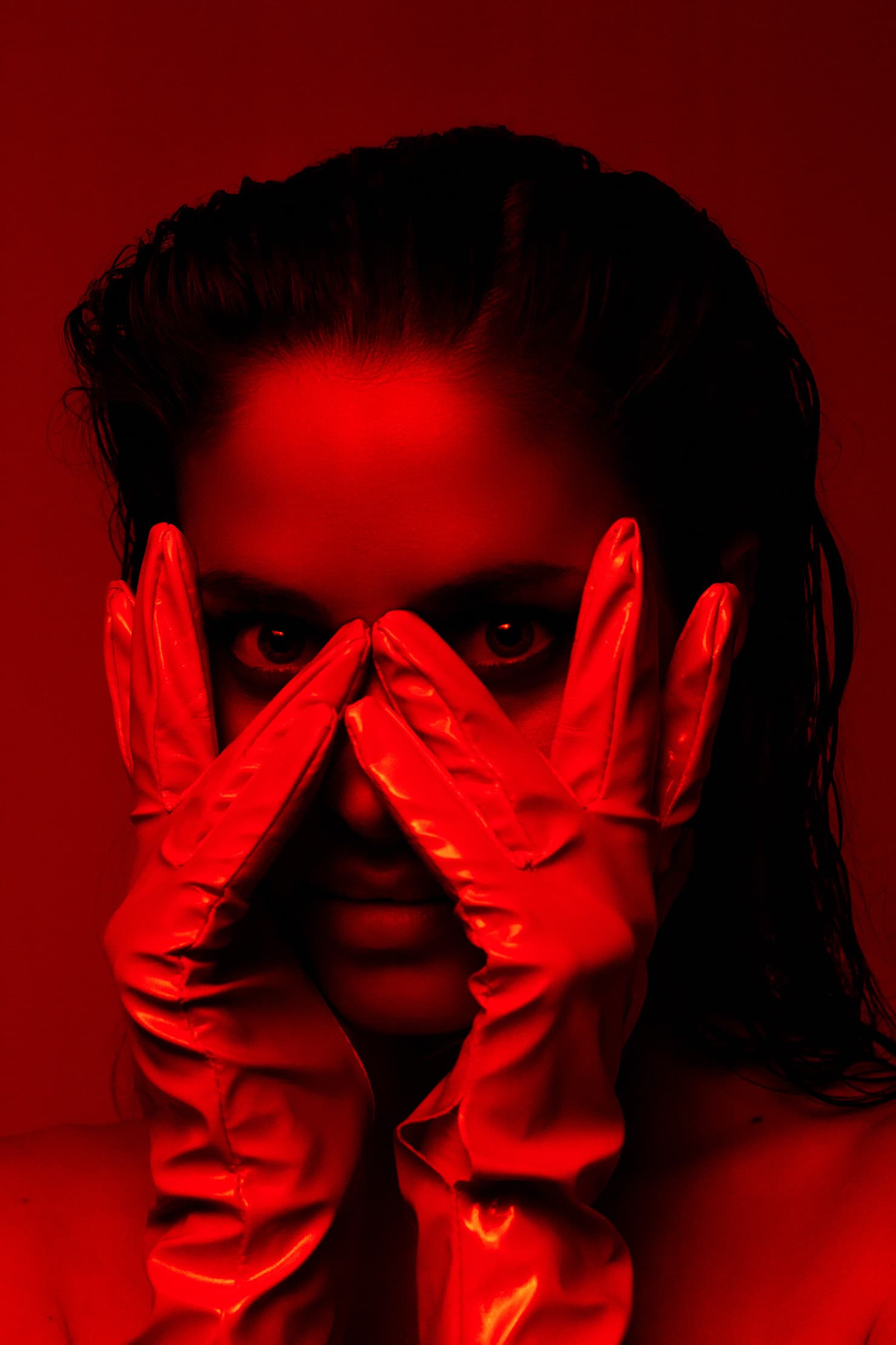 Red-lit portrait of Chloe framing her eyes with satin-gloved hands.