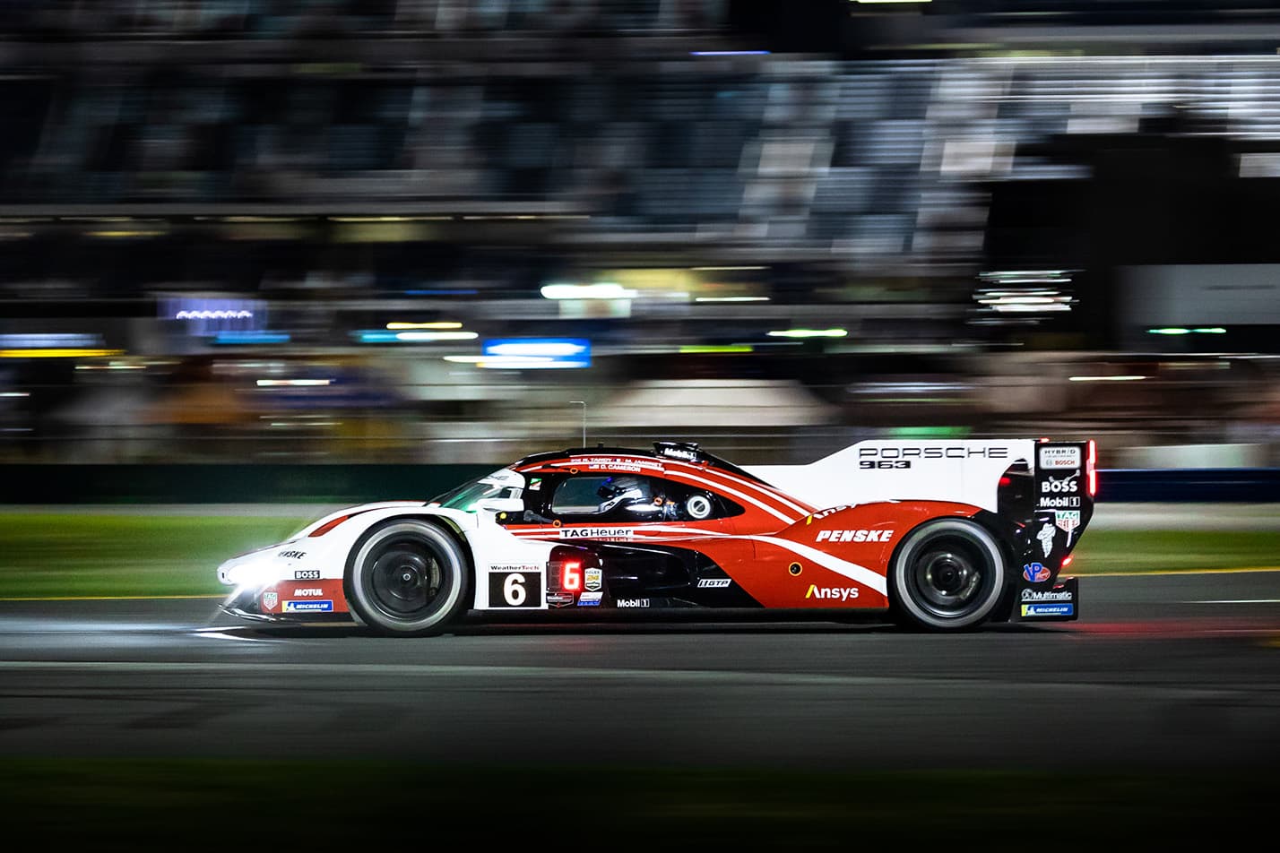 A red and white Porsche 963 racing at night in a panning photograph.