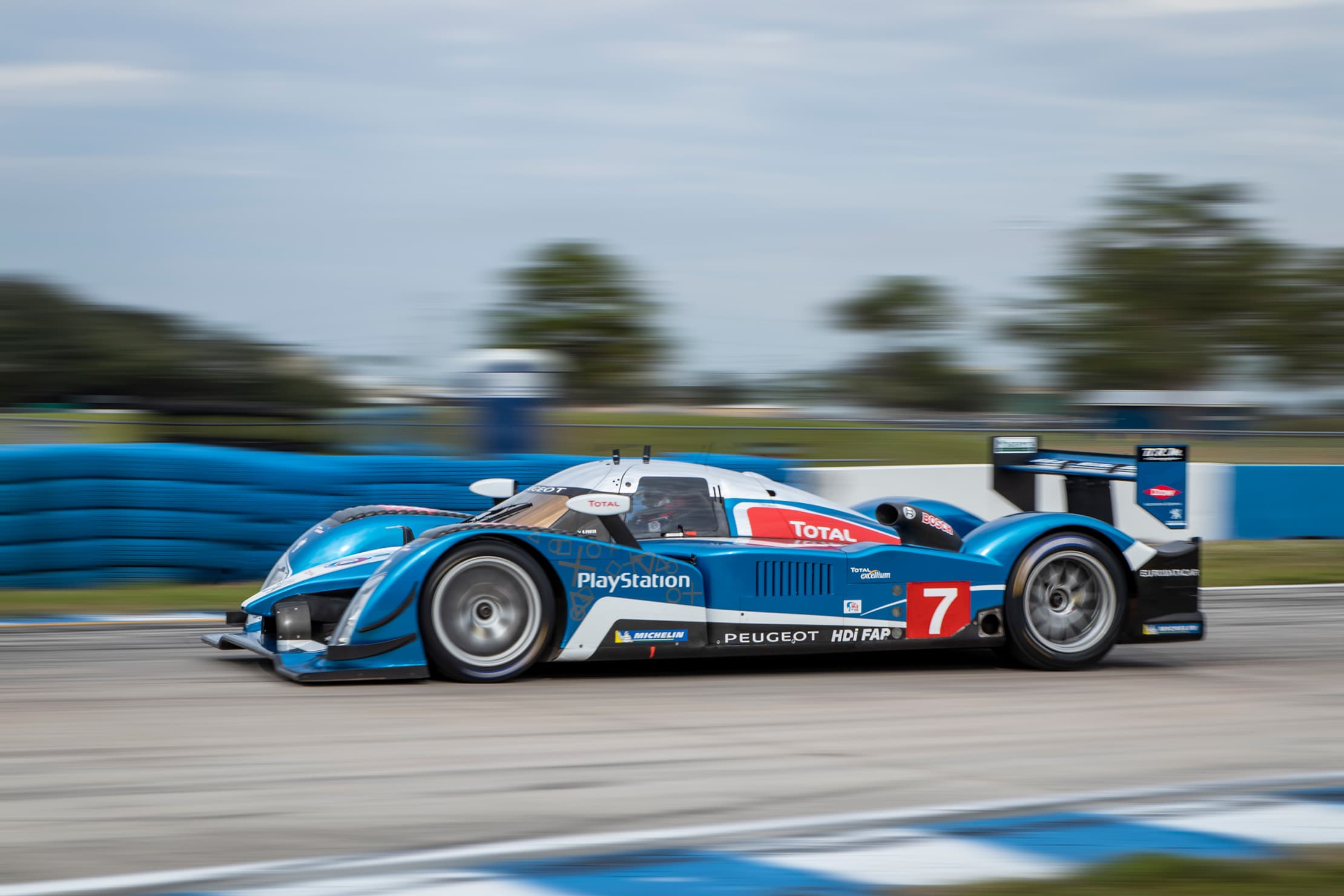 A blue and white number 7 Peugeot prototype in a daylight panning photograph.