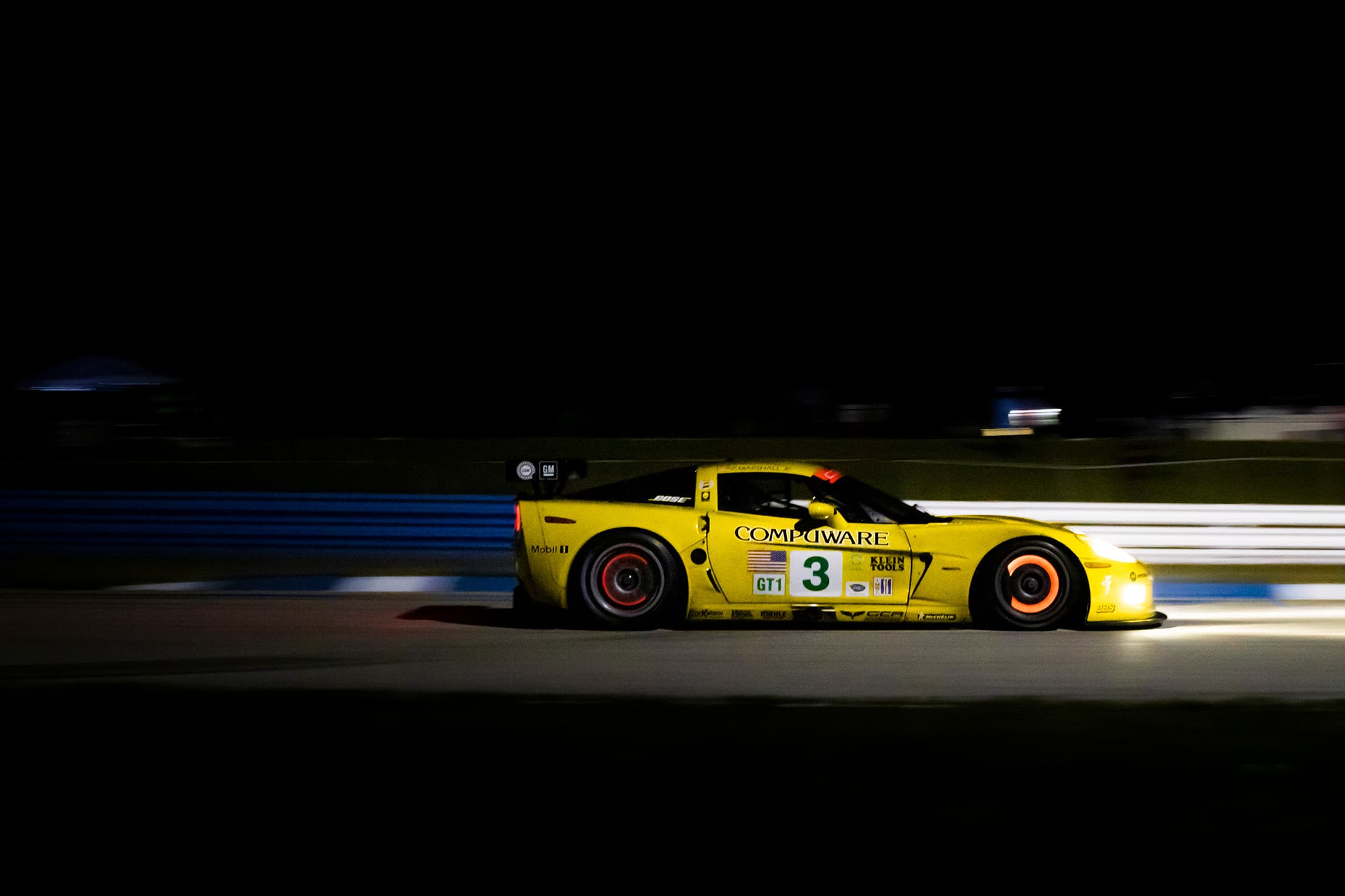 A yellow number 3 Corvette racing side-on at night with glowing brake discs.