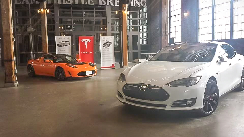 A white Tesla Model S and an orange Tesla Roadster displayed inside Steam Whistle Brewing.