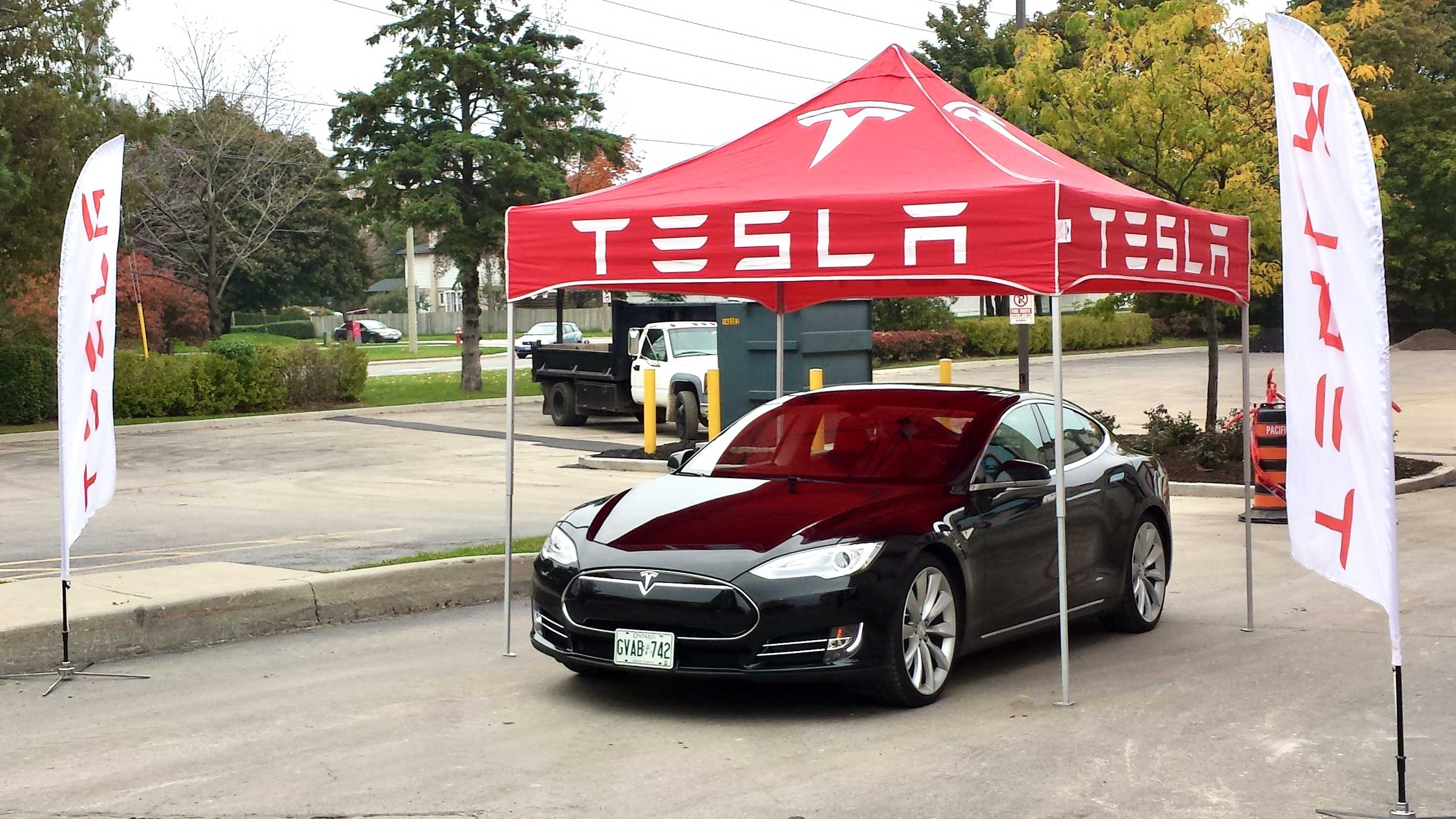 Black Tesla Model S beneath a red Tesla tent in a parking lot